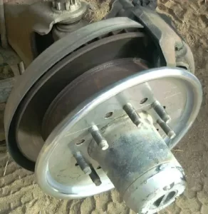 Close up of a vehicles brake drum and wheel hub with lug studs resting on a dusty ground